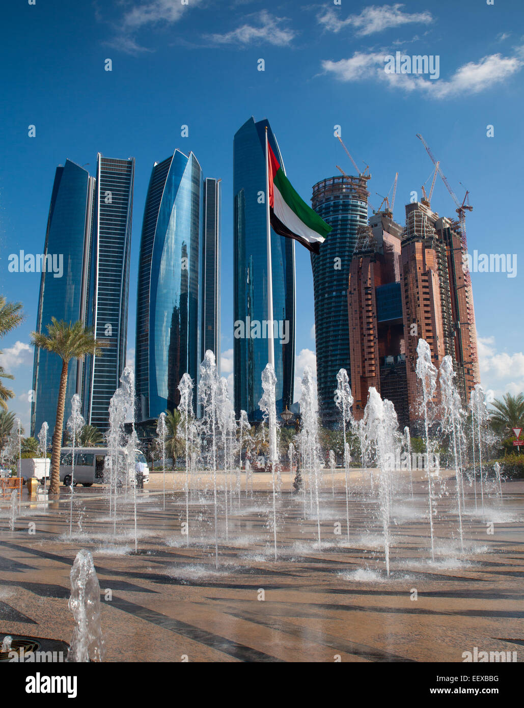 Wolkenkratzer der modernen Abu Dhabi, der Hauptstadt der Vereinigten Arabischen Emirate. Brunnen und Flagge der VAE im Vordergrund. Stadt im Hintergrund. Stockfoto