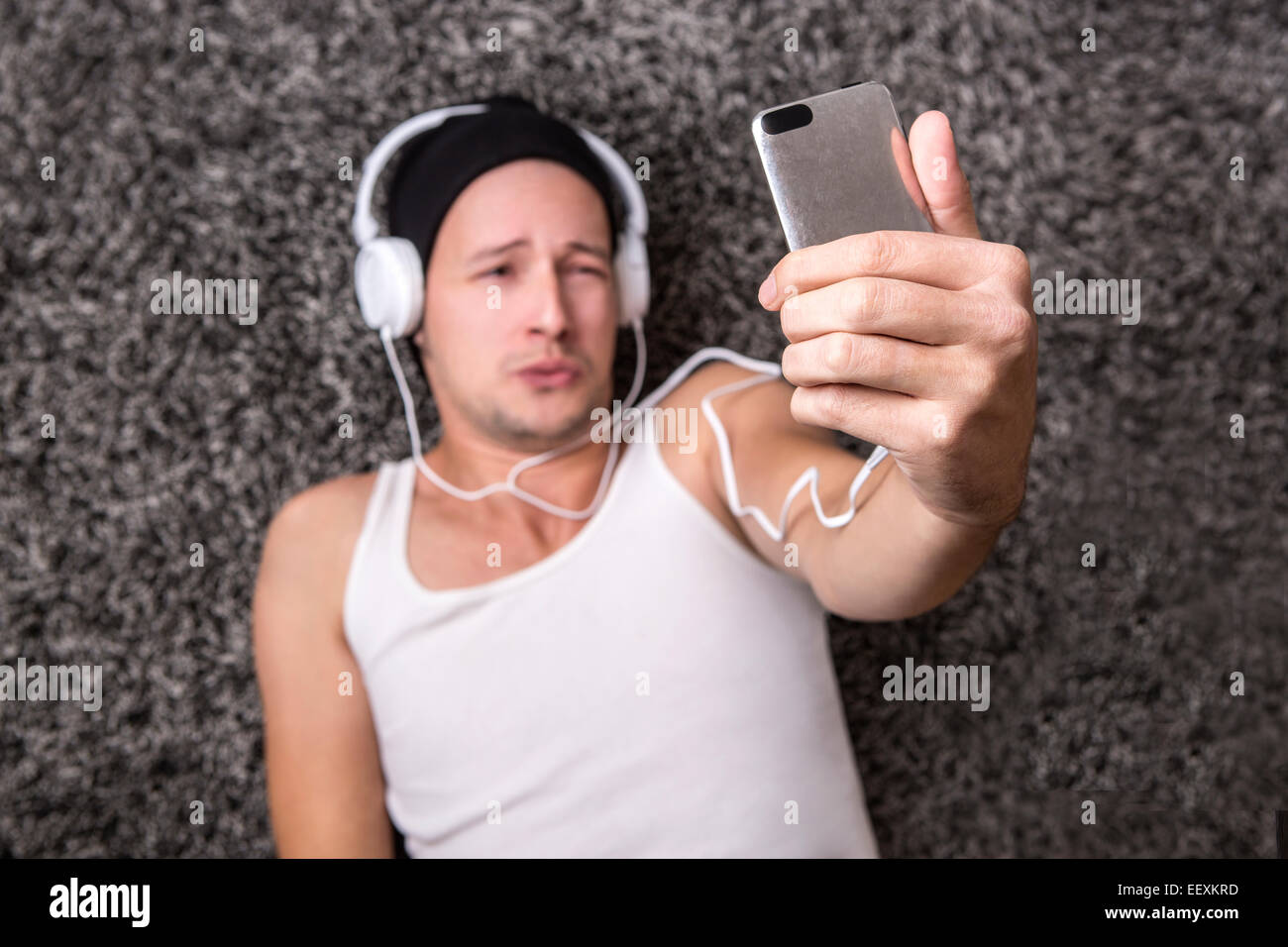 Attraktiver Mann mit Kopfhörern in einem weißen Hemd unglücklich Selfie mit seinem Handy machen Stockfoto