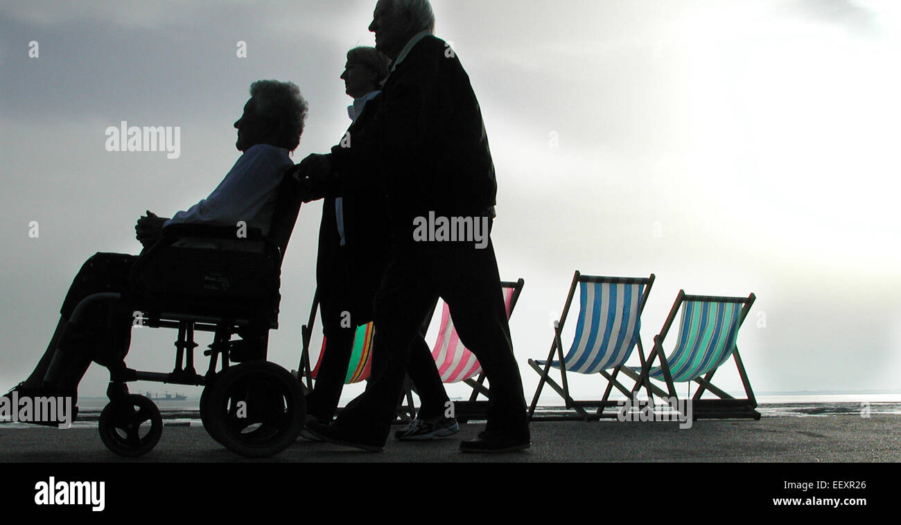 Ältere Rentner gehen mit einem Rollstuhl neben leeren Liegestühlen an der Küste in Southend-on-Sea, Essex, England, UK vorbei Stockfoto