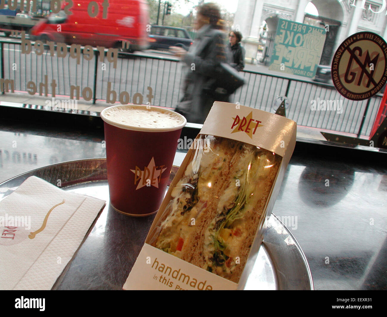 Kaffee und Sandwich auf einem Tisch in einem Restaurant Pret a Manger, mit dem Symbol „No Gentical Modified Food“ im Hintergrund, Marble Arch, London, Großbritannien Stockfoto