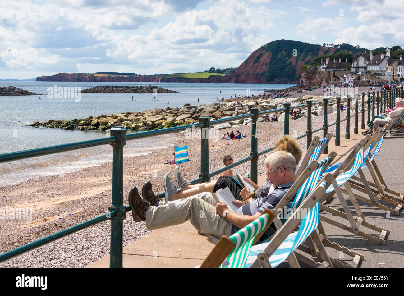 Sidmouth, Devon, UK - Leute sitzen in Liegestühlen am Meer im Sommer Stockfoto