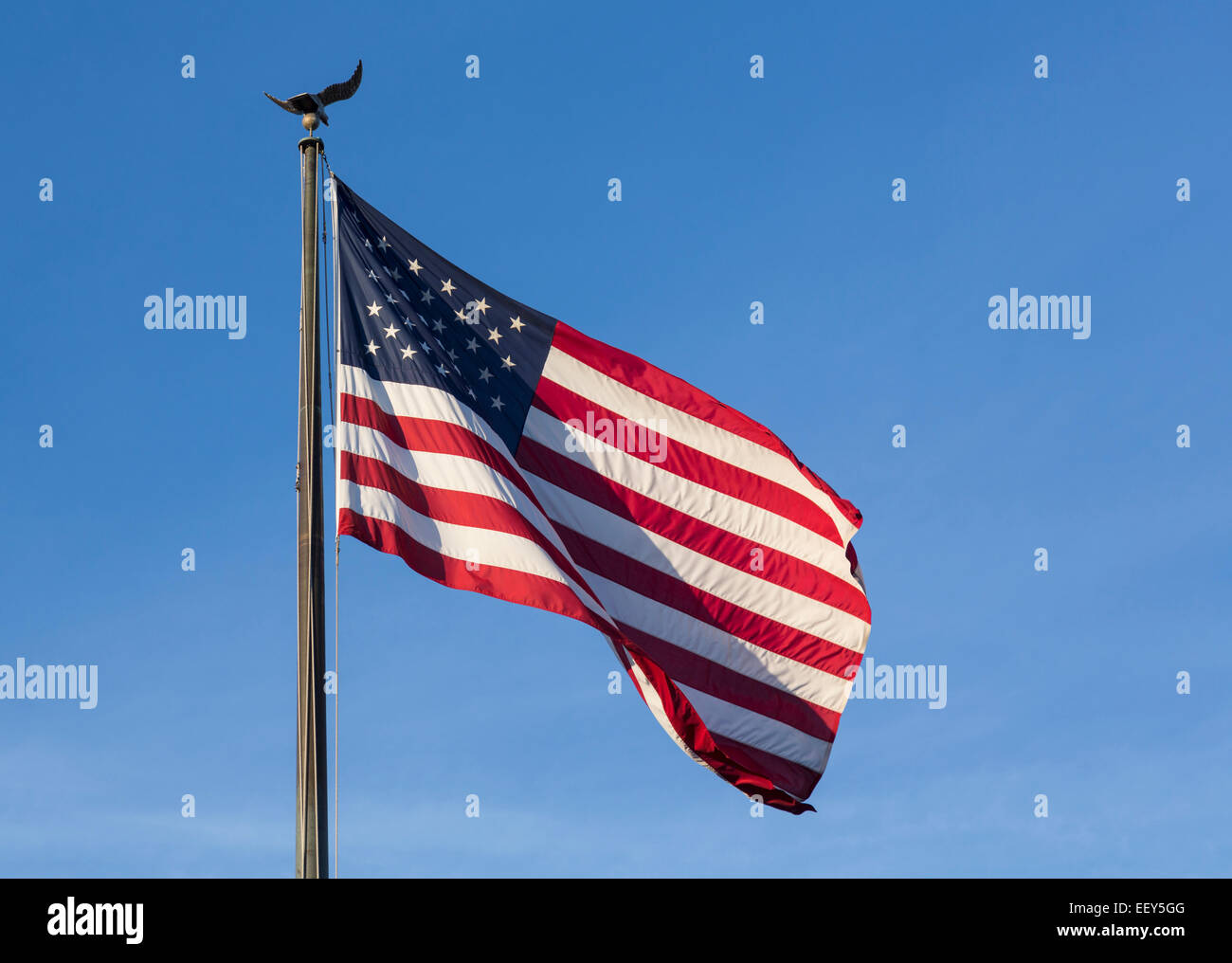 USA-Flagge von Sternen und Streifen mit Adler Fahnenmast gegen blauen Himmel Stockfoto