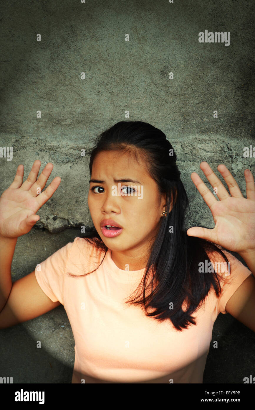 Schockiert asiatische junge Dame stützte sich auf eine Wand mit den Händen oben in einer armen Gegend Blick auf etwas mit der Angst Stockfoto