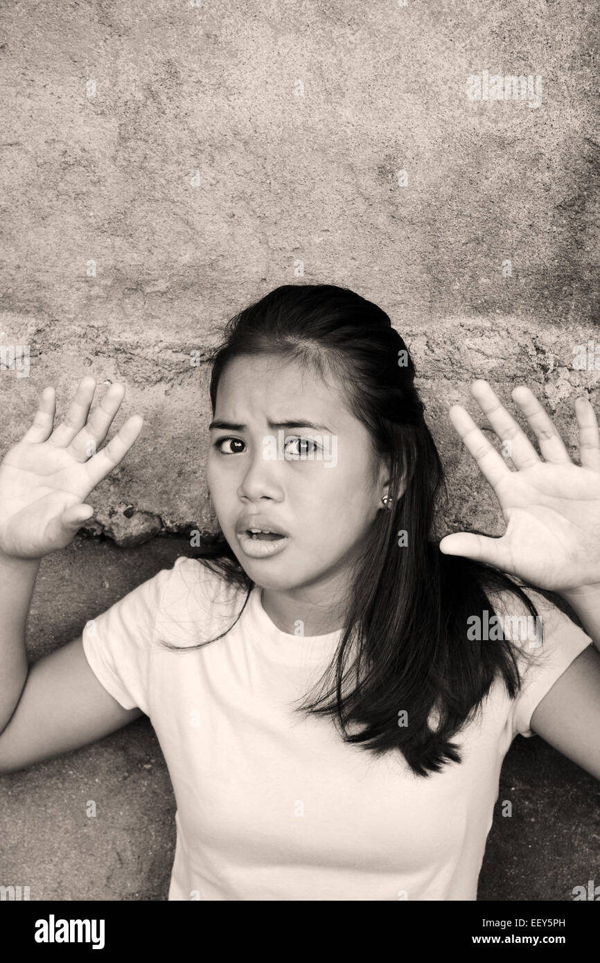 Schockiert asiatische junge Dame stützte sich auf eine Wand mit den Händen oben in einer armen Gegend Blick auf etwas mit der Angst Stockfoto