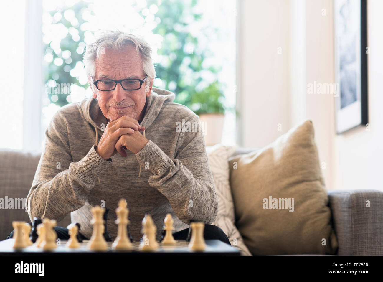 Ältere Mann sitzt im Wohnzimmer und spielt Schach Stockfoto