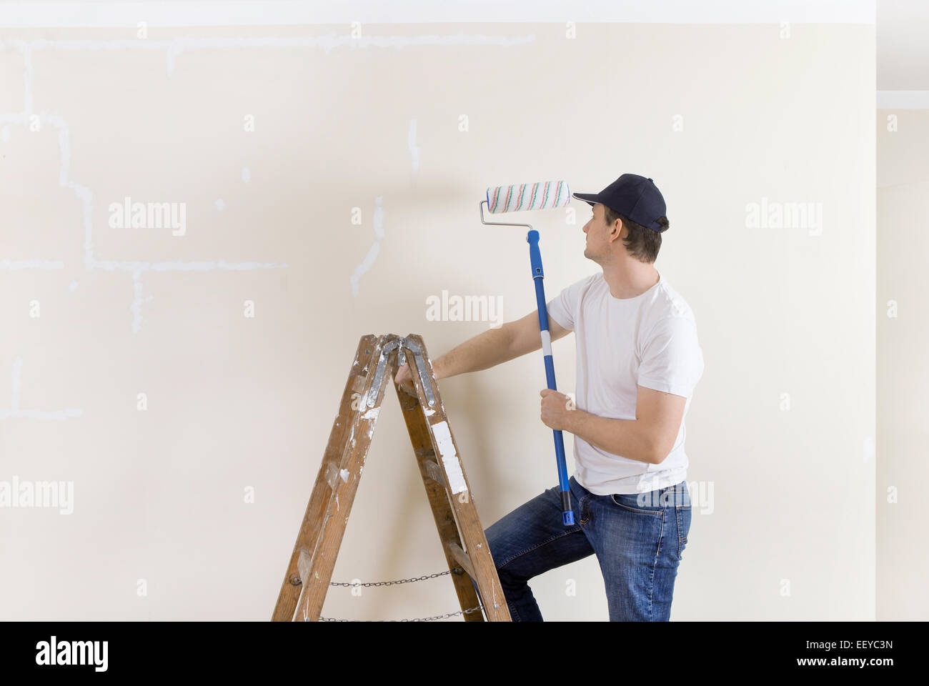 Mann mit Mütze auf einer Leiter stehend und Malerei eine Wand neu Stockfoto