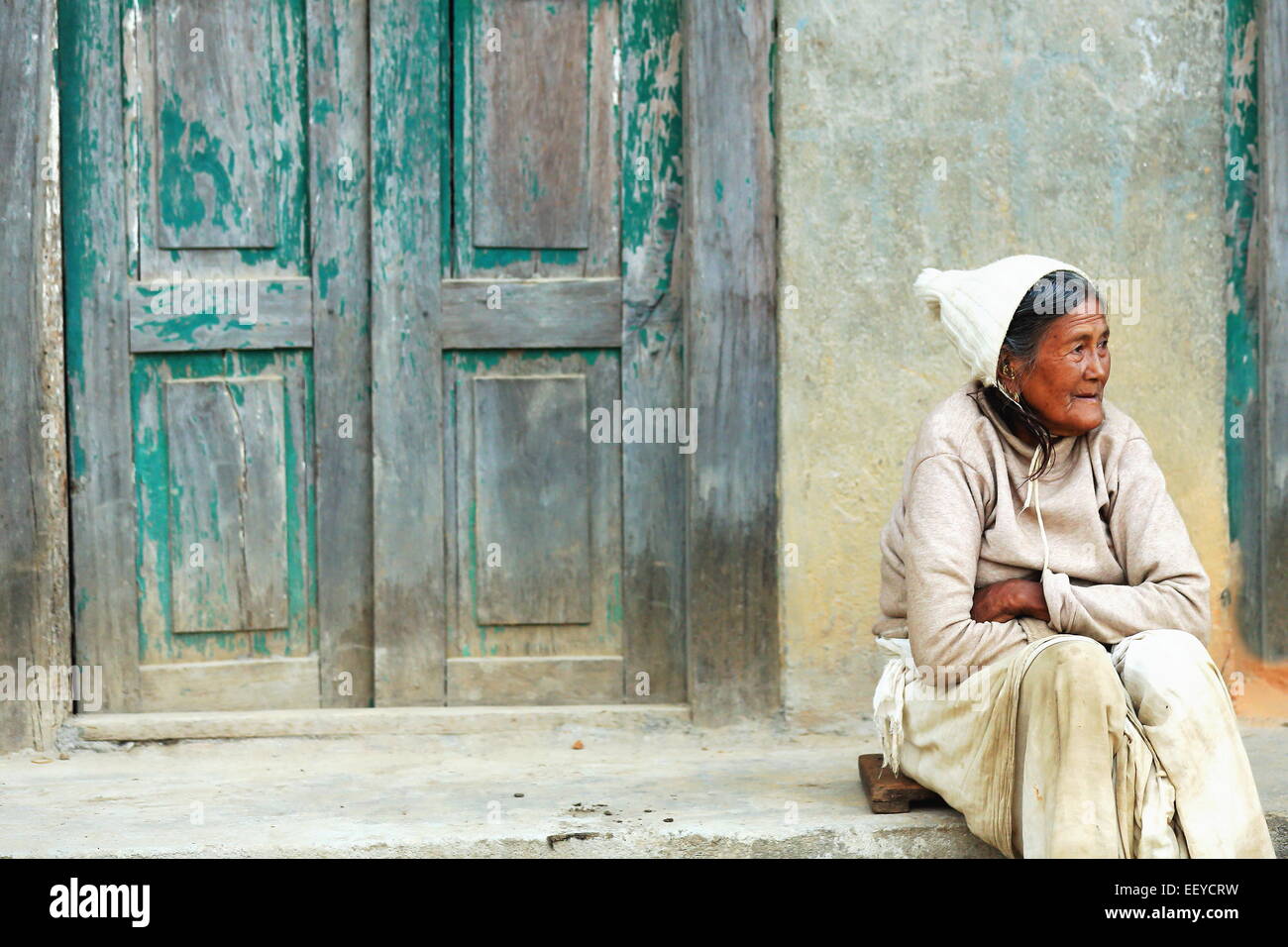 GODAWARI, NEPAL - 15 Oktober: Alte nepalesische Frau sitzt auf dem Boden bevor die Farbe grüne Tür ihres Hauses im Godawari verblasst Stockfoto