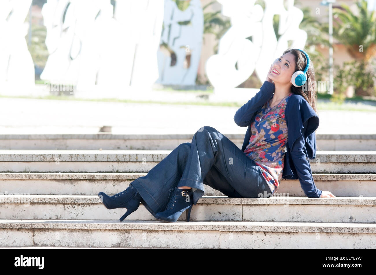 ein Mädchen sitzt auf einer Treppe mit Spaß Musikhören Kopfhörer in Instagram Ton Stockfoto