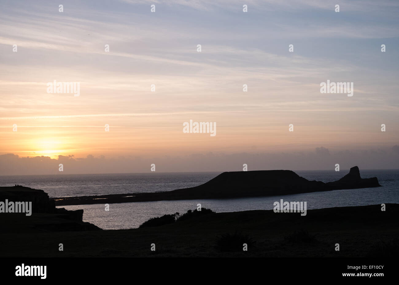 Wanderer-Silhouette bei Sonnenuntergang an einem bitter kalten, sonnigen und windigen Tag in Wurm Kopf, Rhossili Strand Bucht, Halbinsel Gower, Wales, UK, Stockfoto