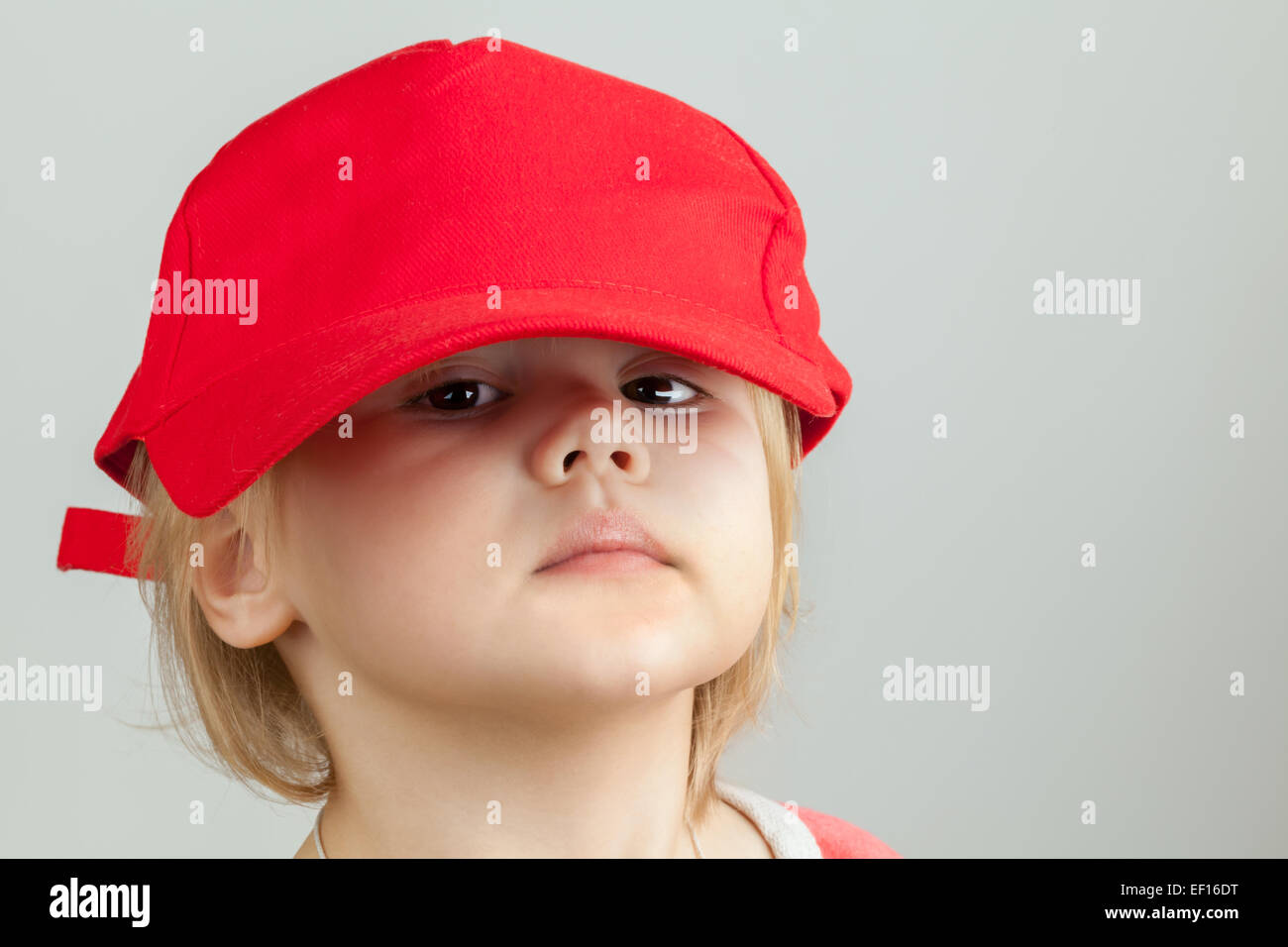 Studio-Porträt der lustige Babymädchen in große rote Baseballmütze über graue Wand Hintergrund Stockfoto
