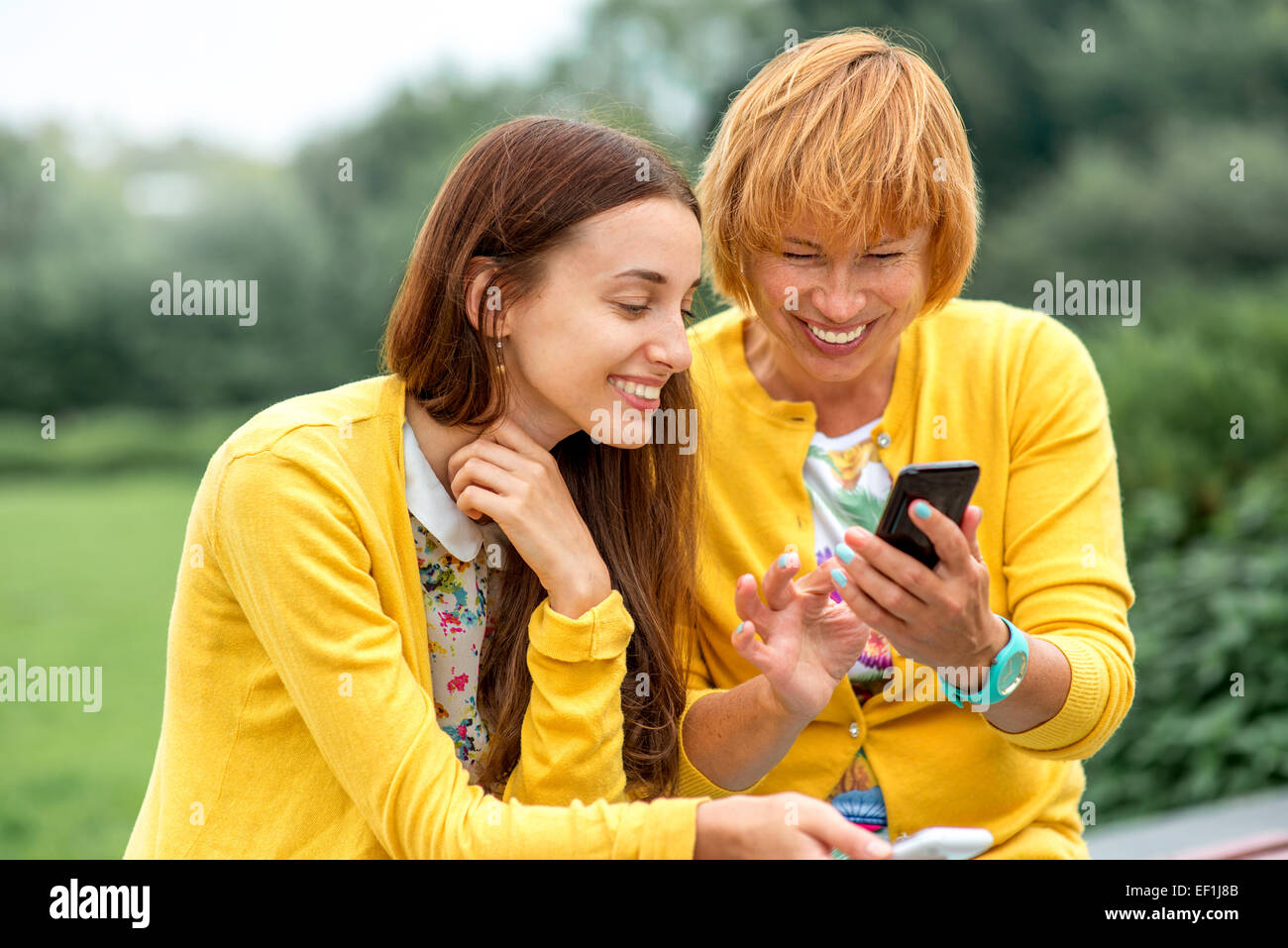Mutter mit ihrer Tochter, die mit Telefon, gekleidet in gelb im park Stockfoto
