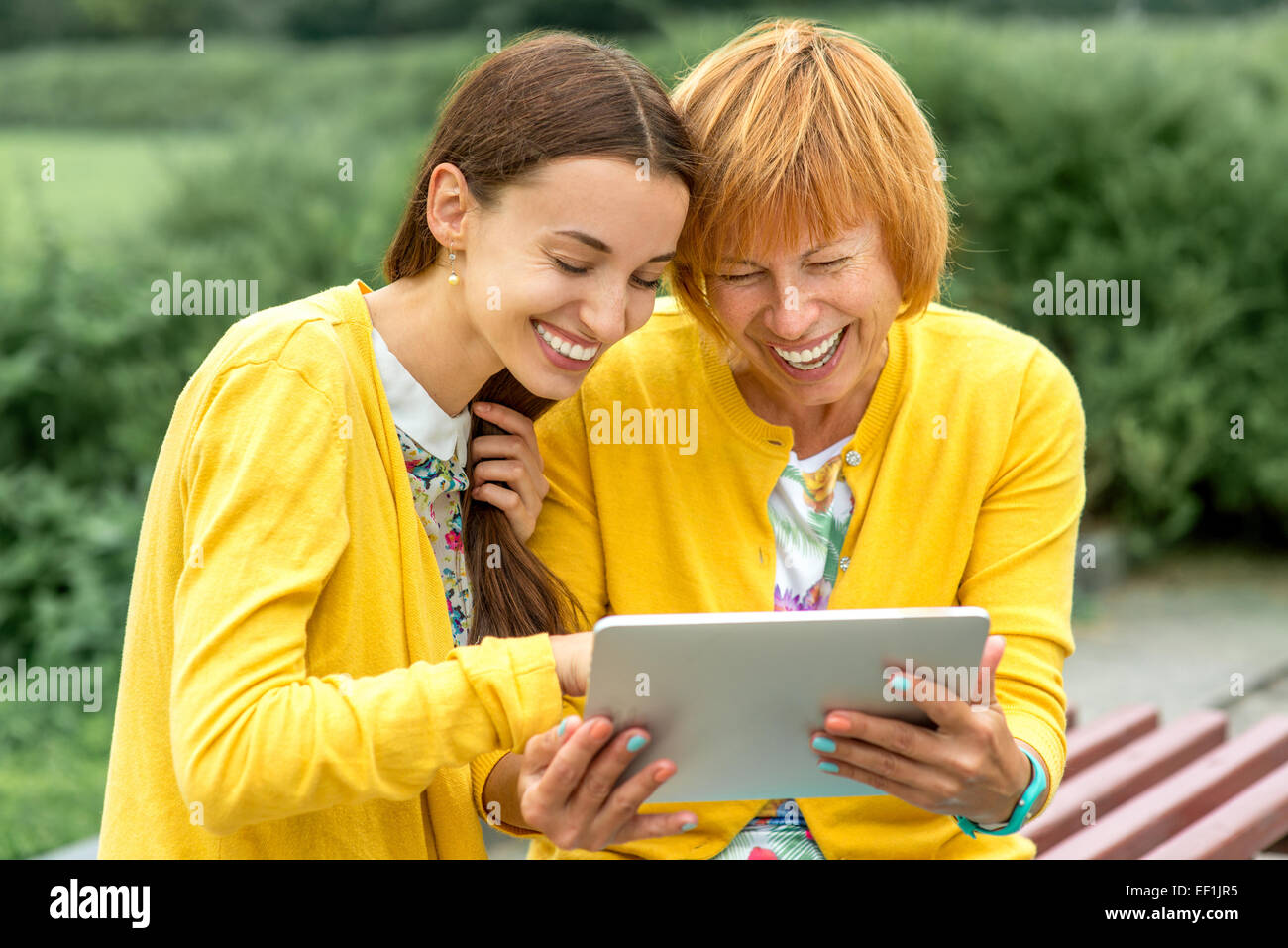 Mutter mit ihrer Tochter mit digital-Tablette gekleidet in gelb im park Stockfoto