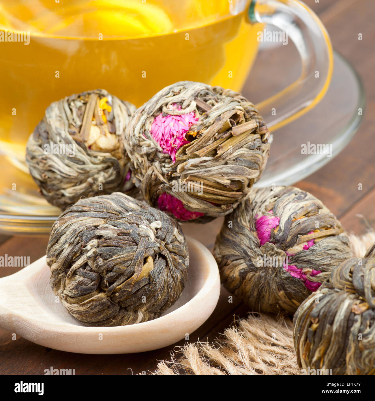 Grüner Tee-Kugeln mit Blumen, Teetasse und Holzlöffel auf Küchentisch Stockfoto