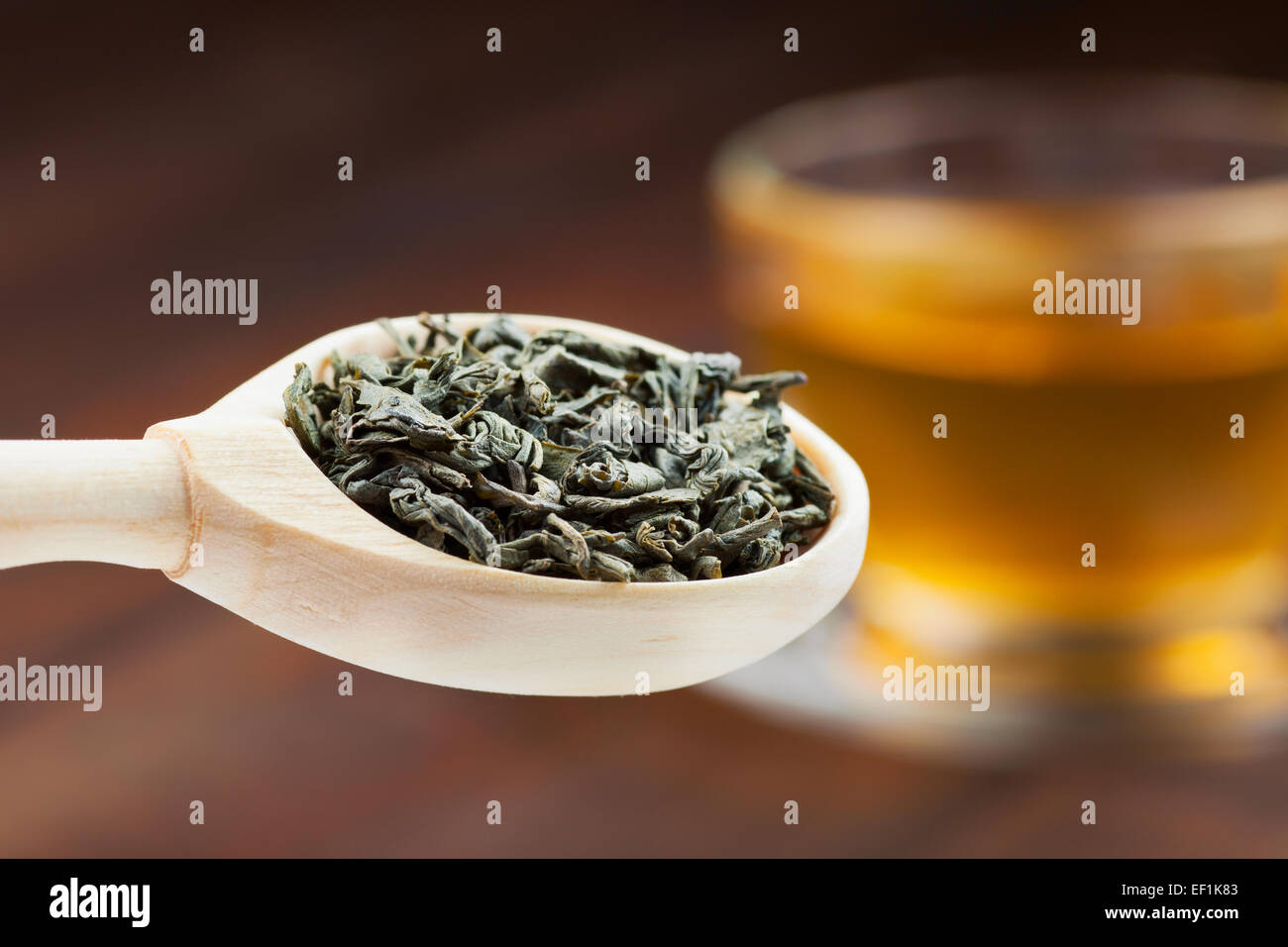 grüner Teeblätter in hölzernen Löffel, Tasse Tee auf Hintergrund Stockfoto