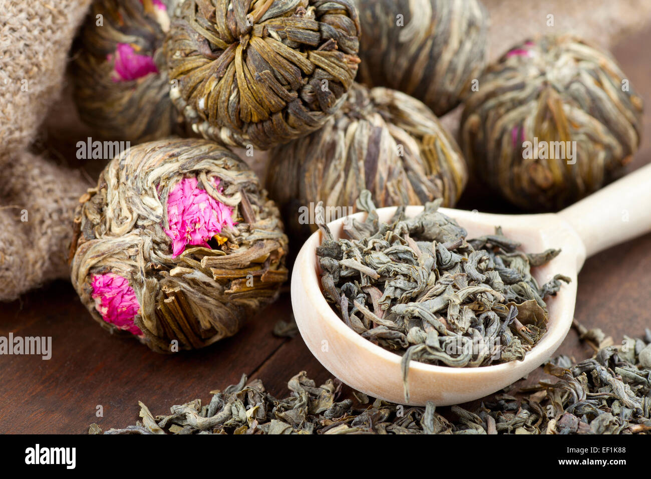 Grüner Tee-Kugeln mit Blumen und Holzlöffel mit Tee am Küchentisch Stockfoto