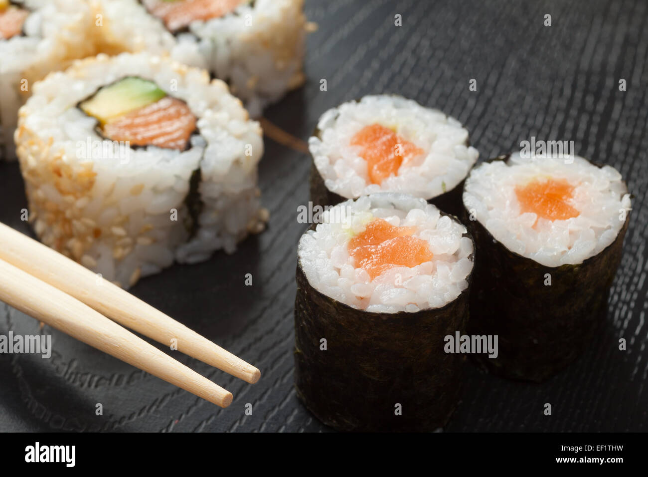 Sushi-Rollen Sortiment auf schwarze Platte und hölzerne Stäbchen Stockfoto