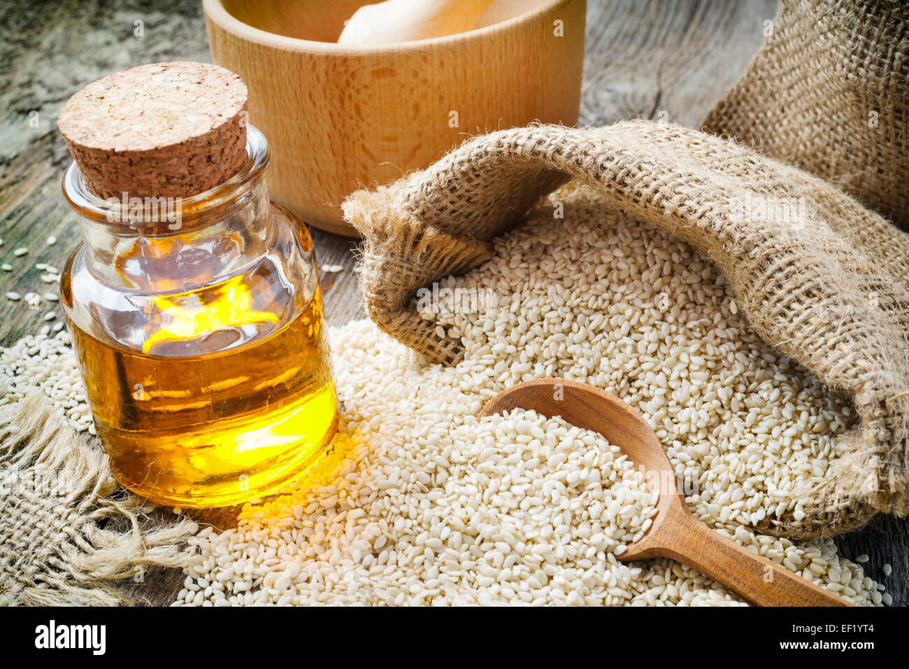 Sesam in Sack und Ölflasche auf rustikalen Holztisch Stockfoto