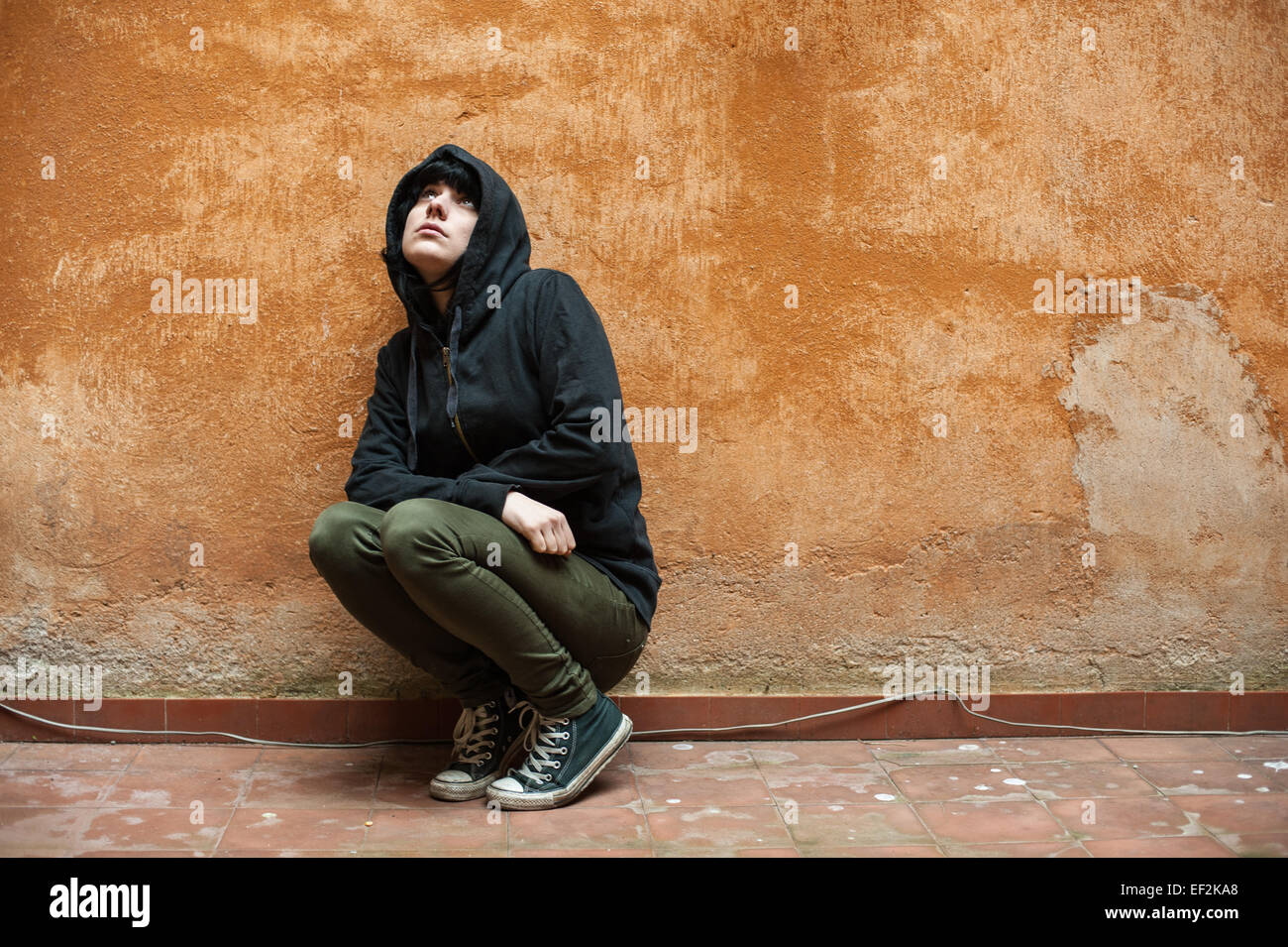 Dunkle traurige junge Frau hockte in der Nähe von städtischen Wand Porträt Stockfoto