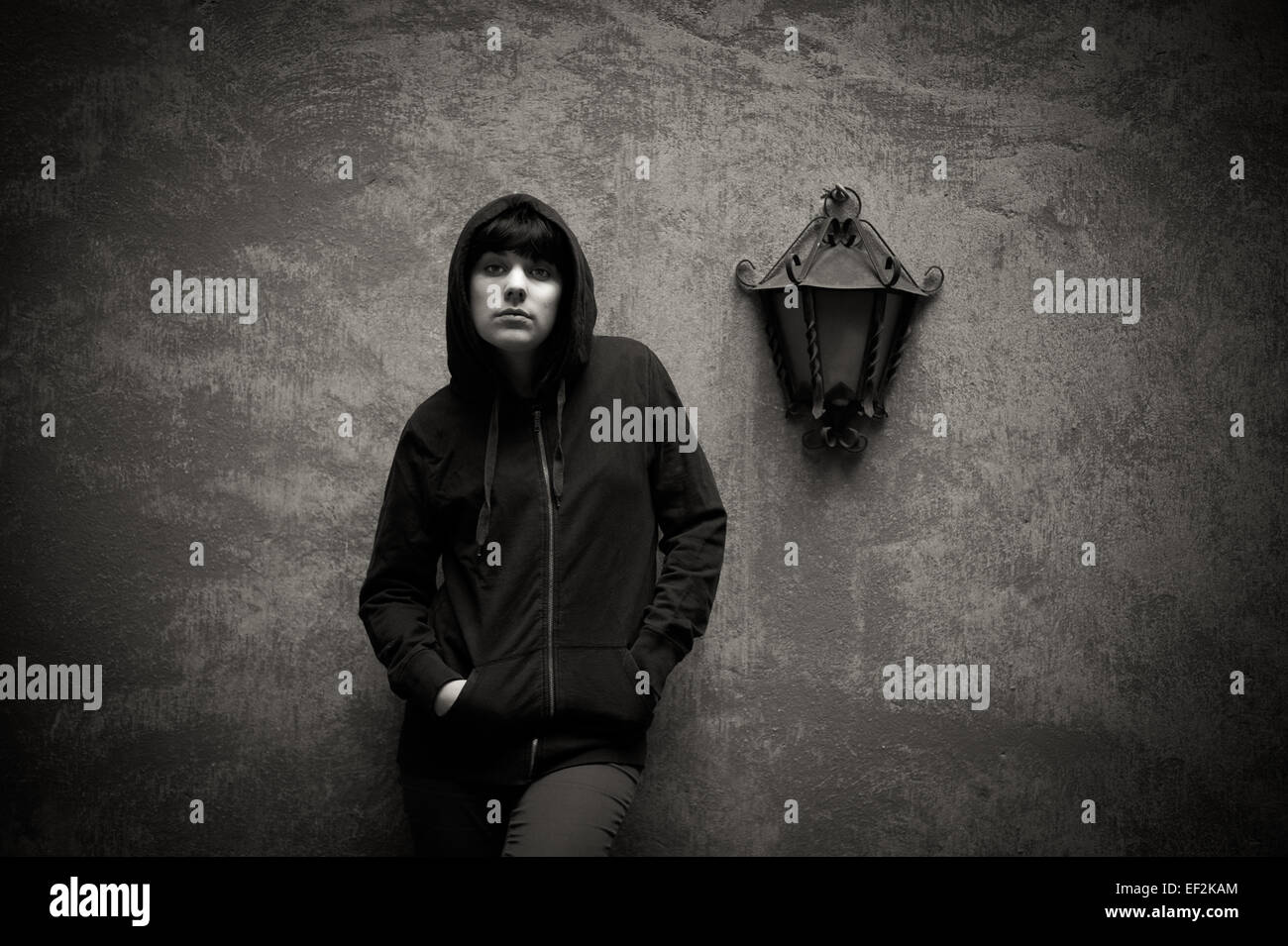 Dunkle junge Frau Freizeitkleidung traurig Stand in der Nähe urbaner Wand in schwarz und weiß Stockfoto