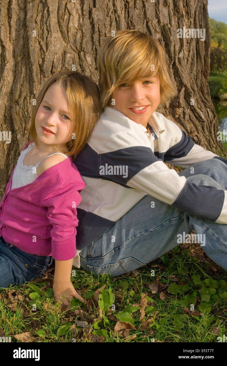 Geschwister sitzen Rücken an Rücken vor großer Baum Stockfoto