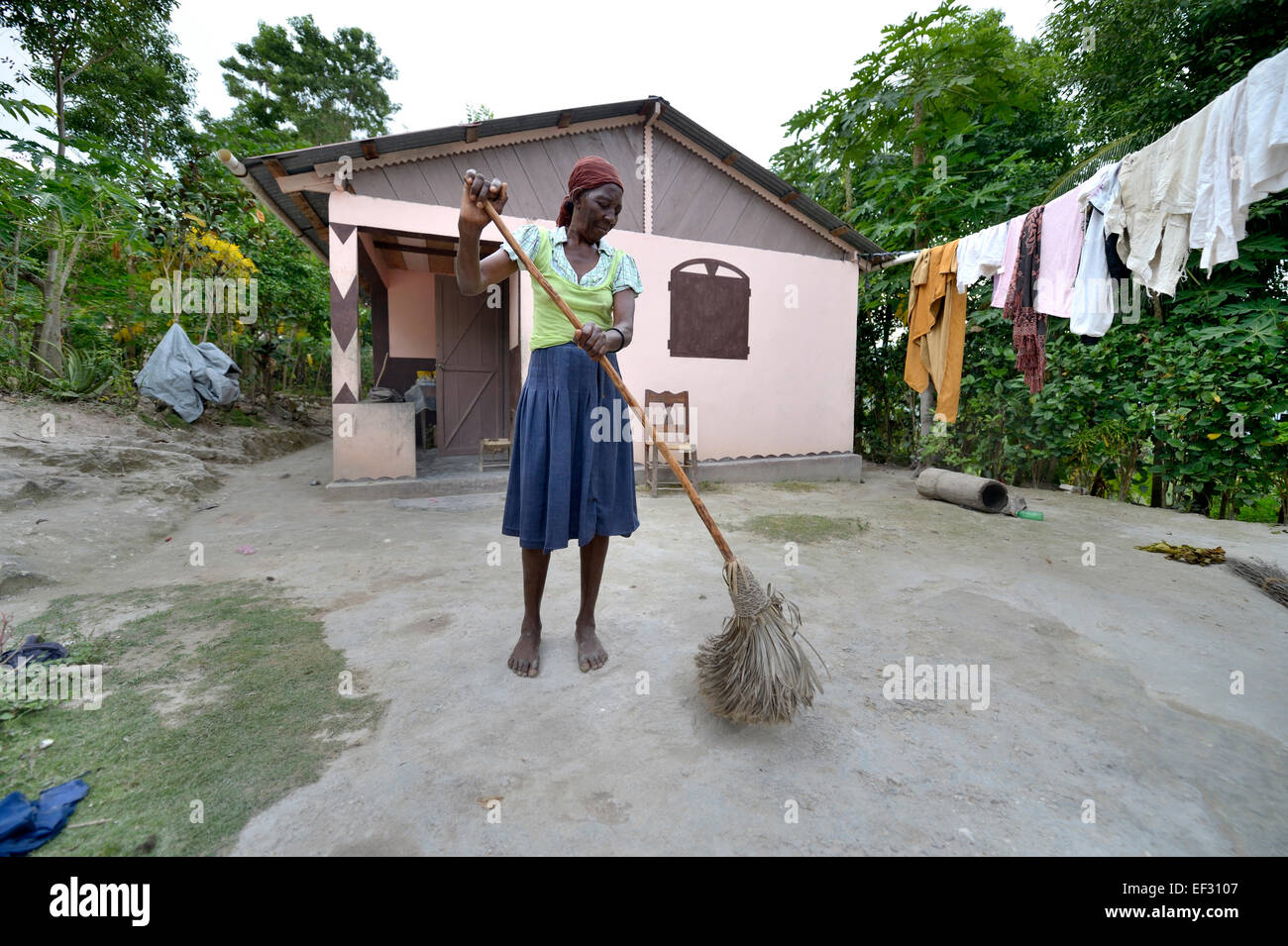 Ältere Frau fegt den Hof vor dem Haus, die sie von einer Hilfsorganisation nach dem 2010 erhielt Stockfoto