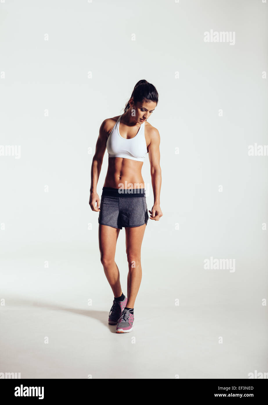 In voller Länge Portrait von Fit junge Frau im Sport tragen blickte auf grauem Hintergrund stehend. Muskuläre Fitness-Modell. Stockfoto