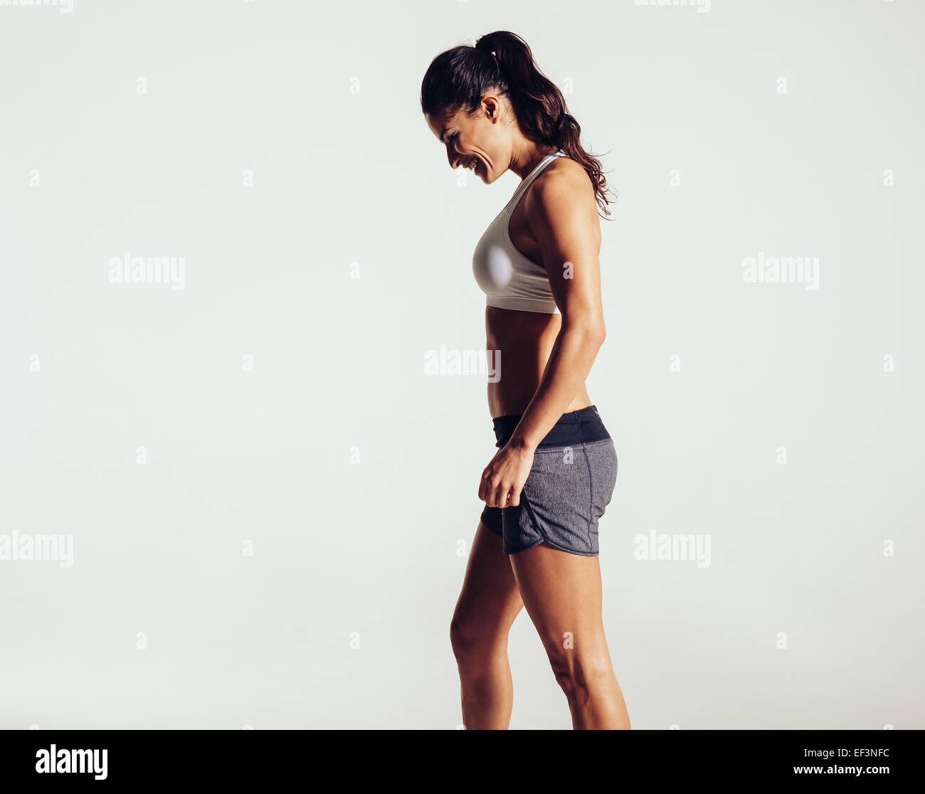Seitenansicht der glückliche junge Frau in Sportkleidung vor grauem Hintergrund. Fitness-Frau lachend. Stockfoto