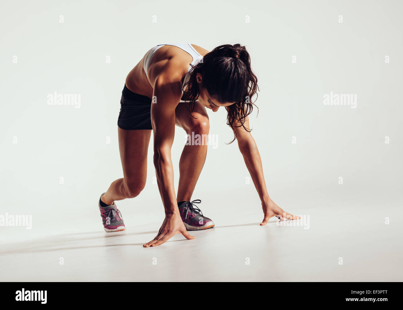 Passen Sie Sportlerin startbereit auf grauem Hintergrund. Frauen Fitness-Modell für einen Sprint vorbereiten. Stockfoto