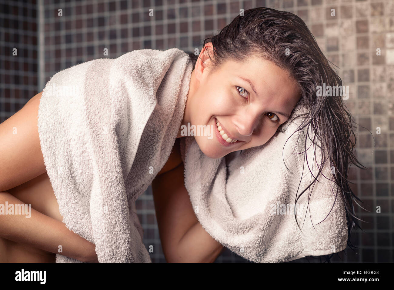 Lächelnde Frau mit nassen Haaren stehen in einer Dusche mit grauen Mosaik Fliesen selbst auf ein sauberes weißes Handtuch trocknen Stockfoto
