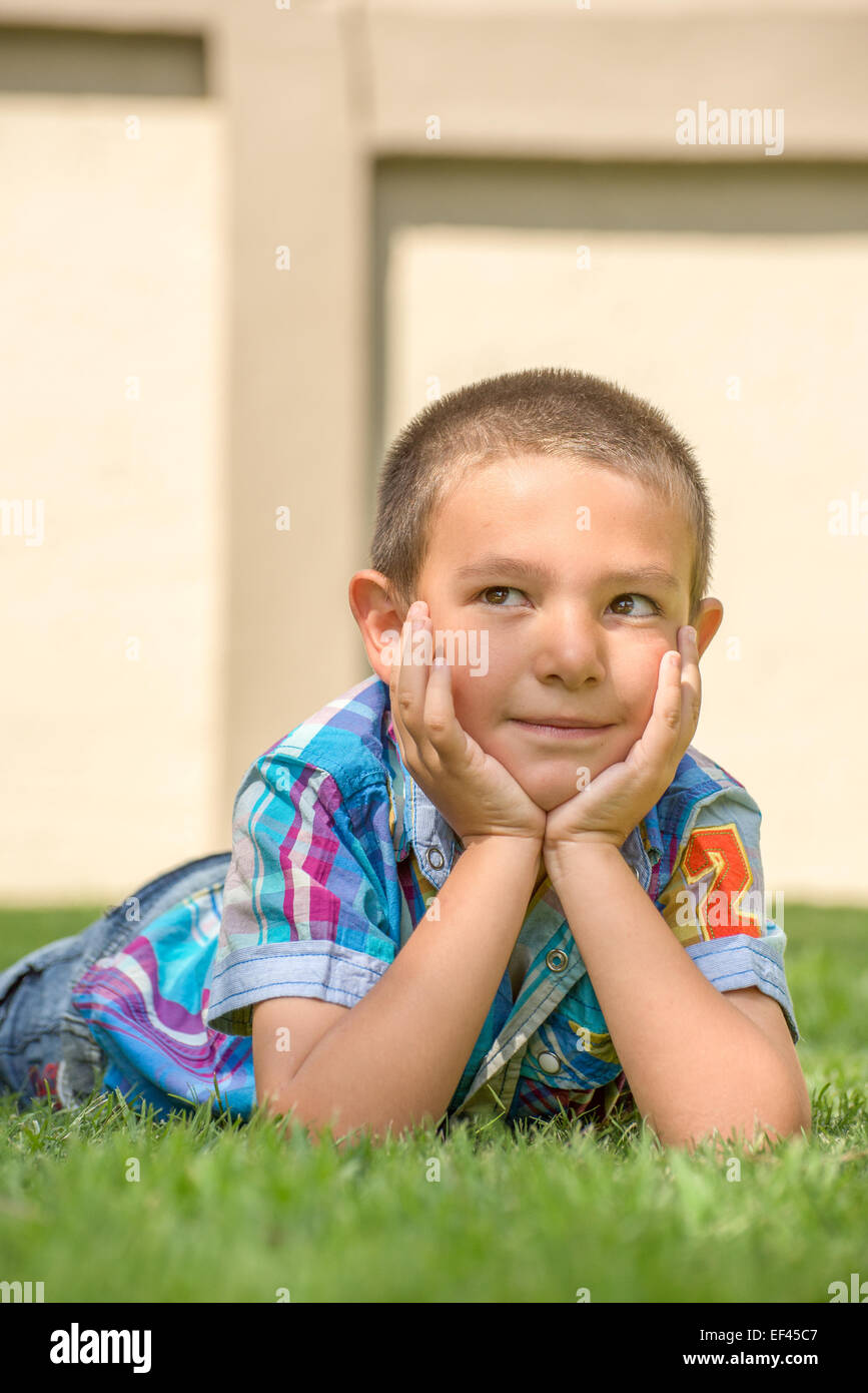 Junge liegend auf dem Rasen an einem schönen Frühlingstag mit Kopf in Händen, als ob Tagträumen. Stockfoto