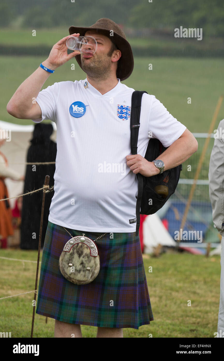 Ein Mann in einem schottischen Kilt trägt eine England Fußball-Shirt und ein Bierchen getrunken, während Ereignisse bei Bannockburn Live, Schottland. Stockfoto