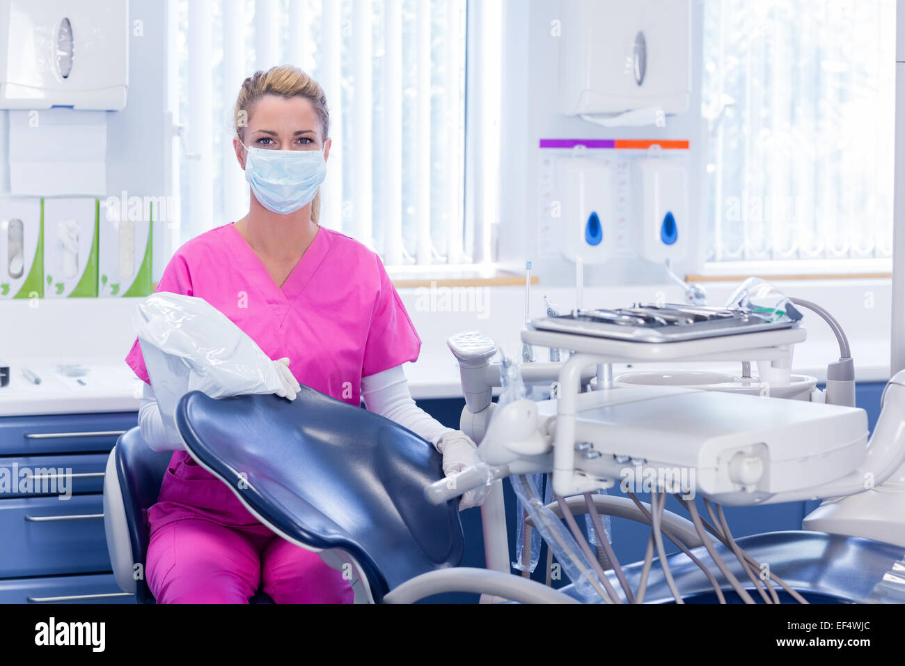 Zahnarzt in rosa scheuert, Blick in die Kamera neben Stuhl Stockfoto