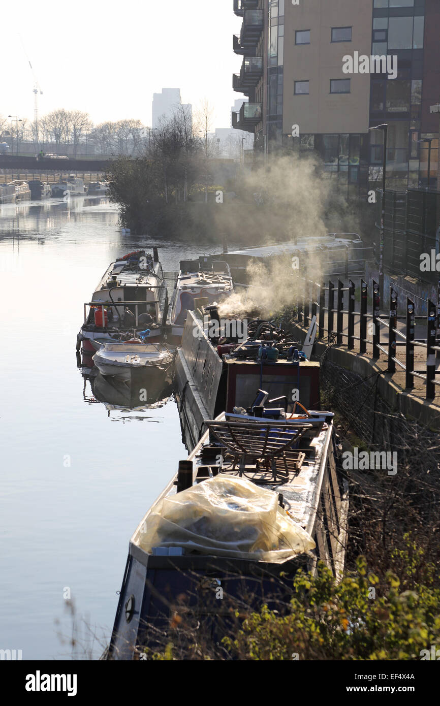 Traditionelle schmale Boote vertäut am Fluss Lee-Navigation in East London im Winter. Rauch steigt aus einem Heizofen zeigt Stockfoto