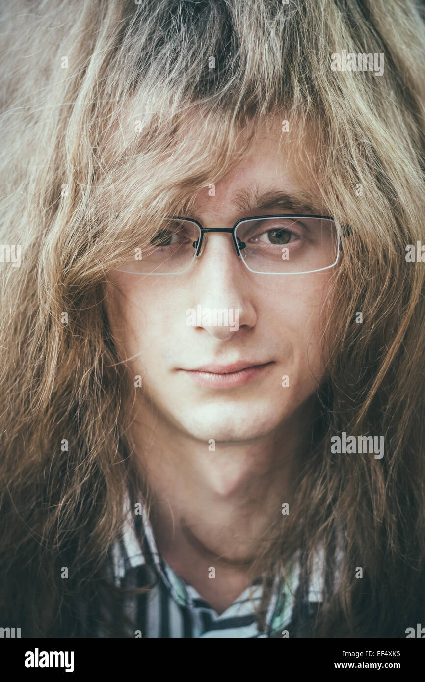 Porträt von Rock Star jungen Mann Mann mit Brille und langen Haaren lächelnd und Blick in die Kamera Stockfoto