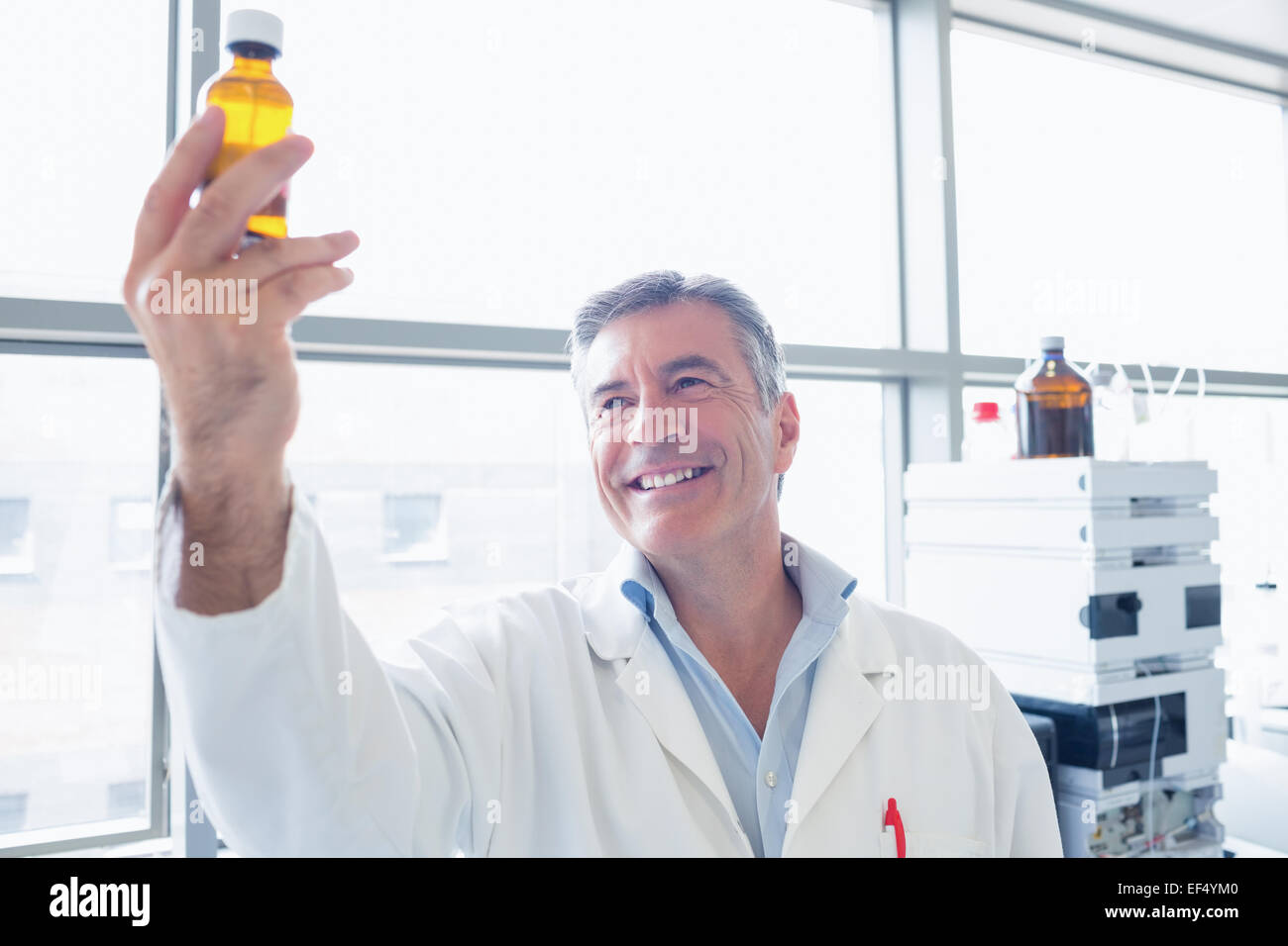 Wissenschaftler im Laborkittel mit einer chemischen Flasche lächelnd Stockfoto