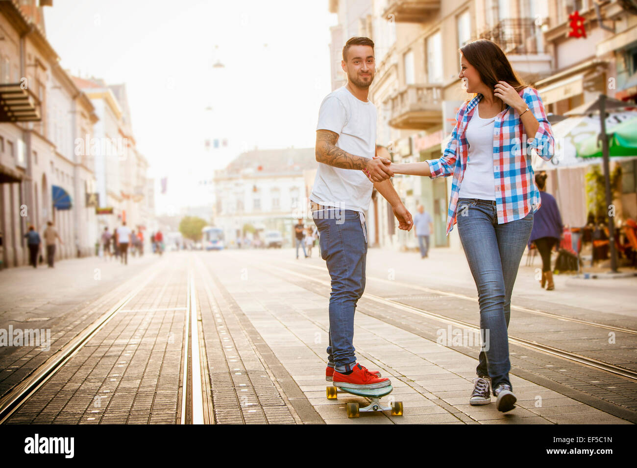Junger Mann Skateboarden auf Stadtstraße, Frau Unterstützung Stockfoto