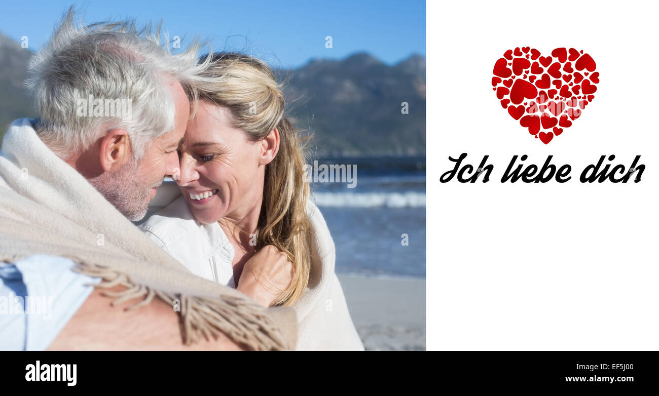 Zusammengesetztes Bild des lächelnden paar sitzt am Strand unter Decke Stockfoto