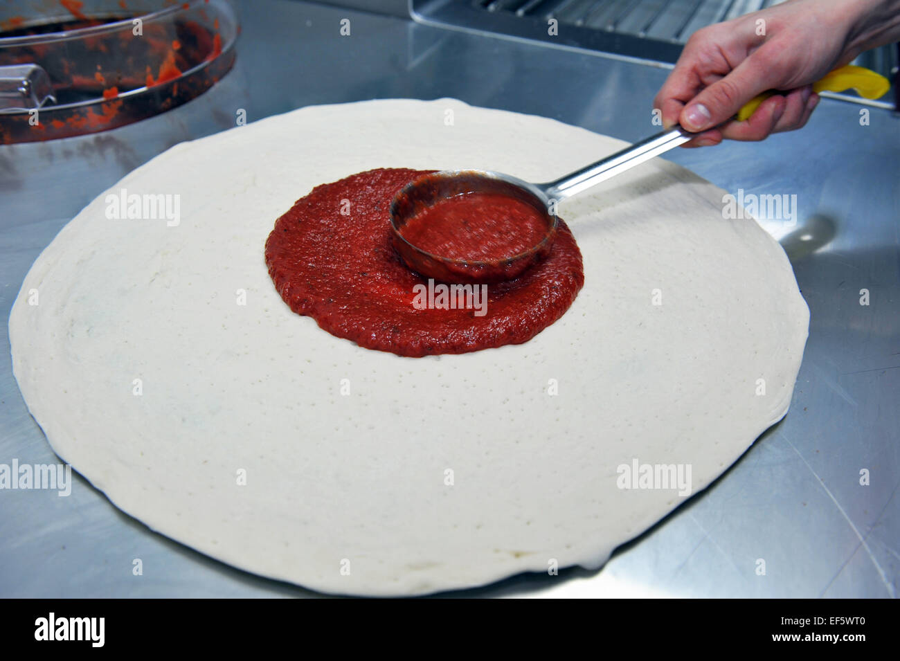 Pizzateig in einem Fast-Food-Restaurant Tomatensauce hinzufügen. Stockfoto
