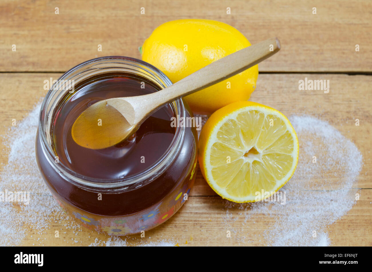 Glas mit dunklem Honig einen Holzlöffel und Zitronen auf einem Tisch Stockfoto