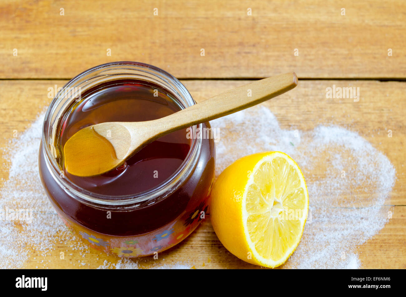 Jar von dunklem Honig einen Holzlöffel und eine Zitrone auf einem Tisch Stockfoto