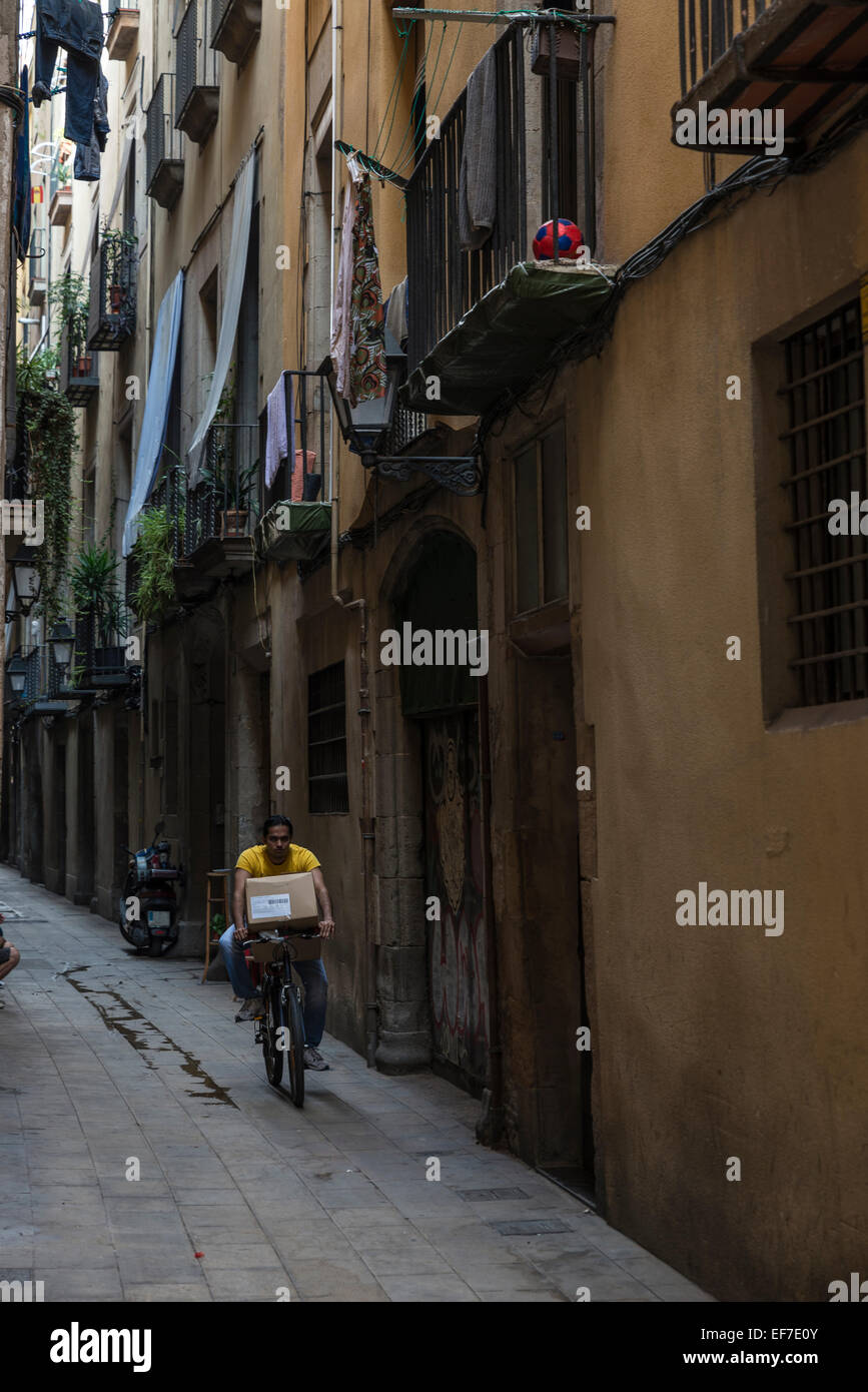 Junger Mann auf einem Fahrrad mit einem Paket auf einer Straße in der Altstadt von Barcelona Stockfoto