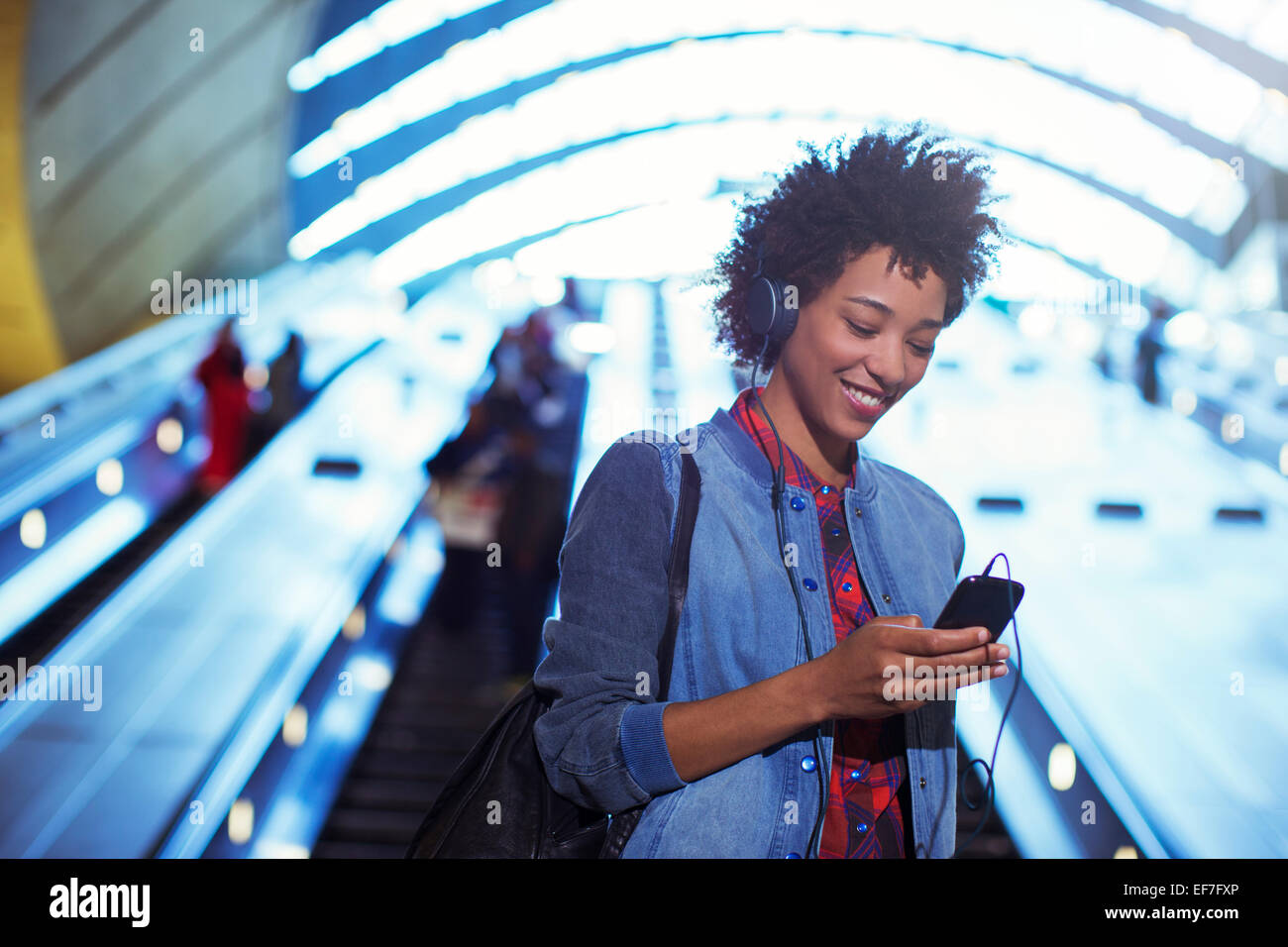 Lächelnde Frau anhören von MP3-Player auf Rolltreppe Stockfoto