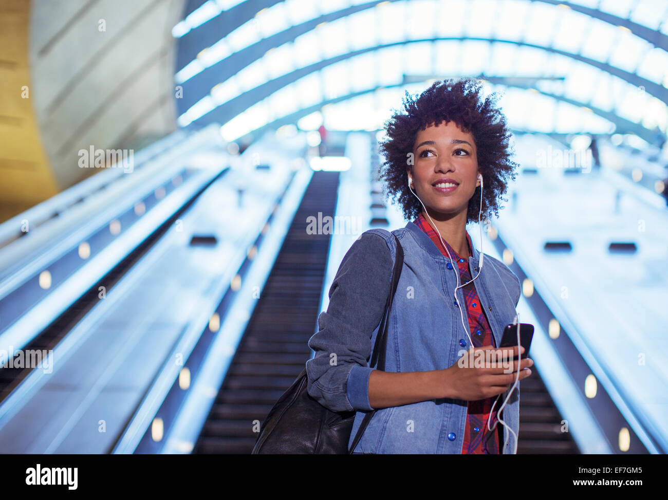 Frau anhören Ohrhörer auf Rolltreppe Stockfoto