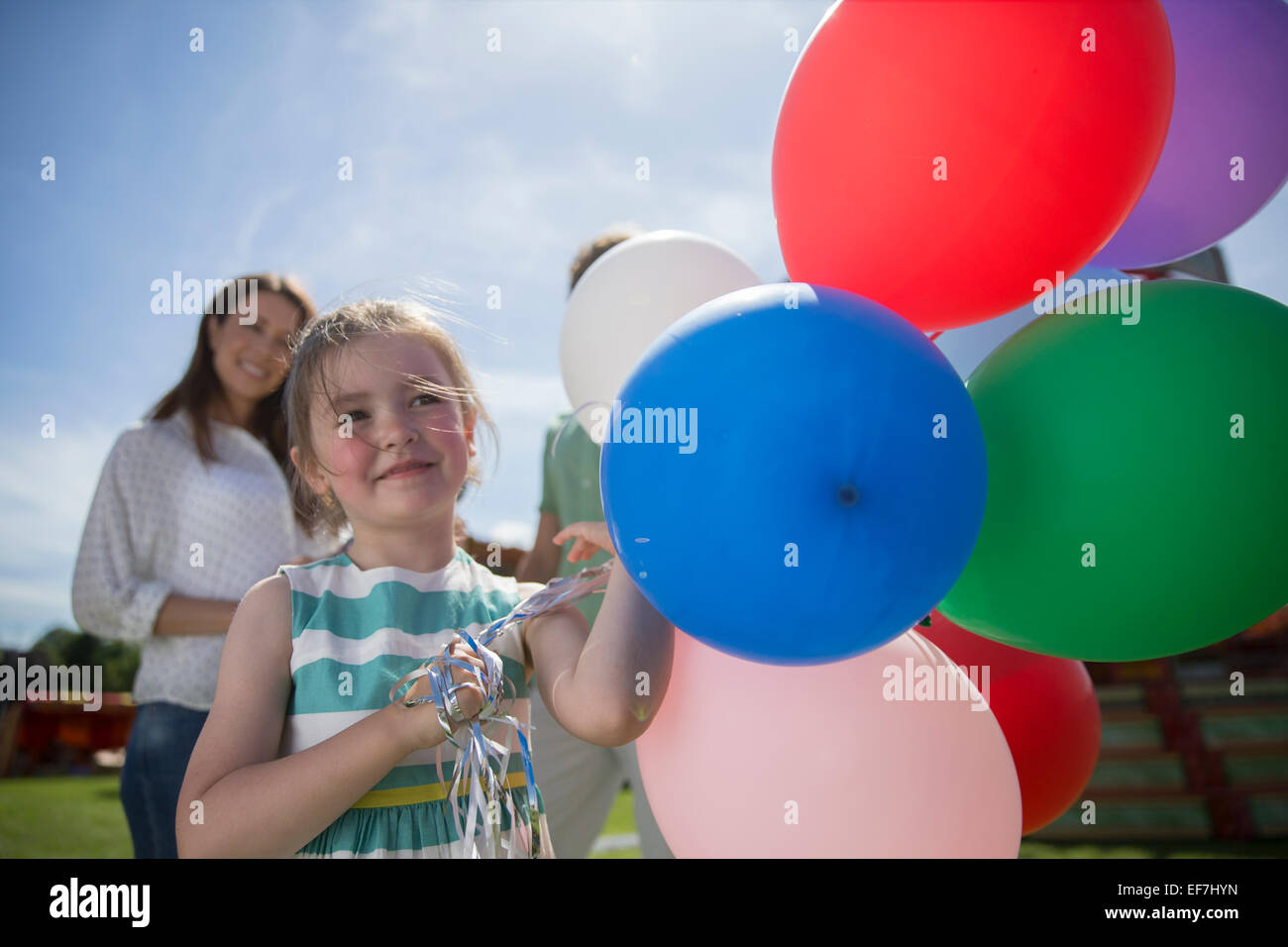 Junges Mädchen hält Haufen bunter Luftballons am sonnigen Tag Stockfoto