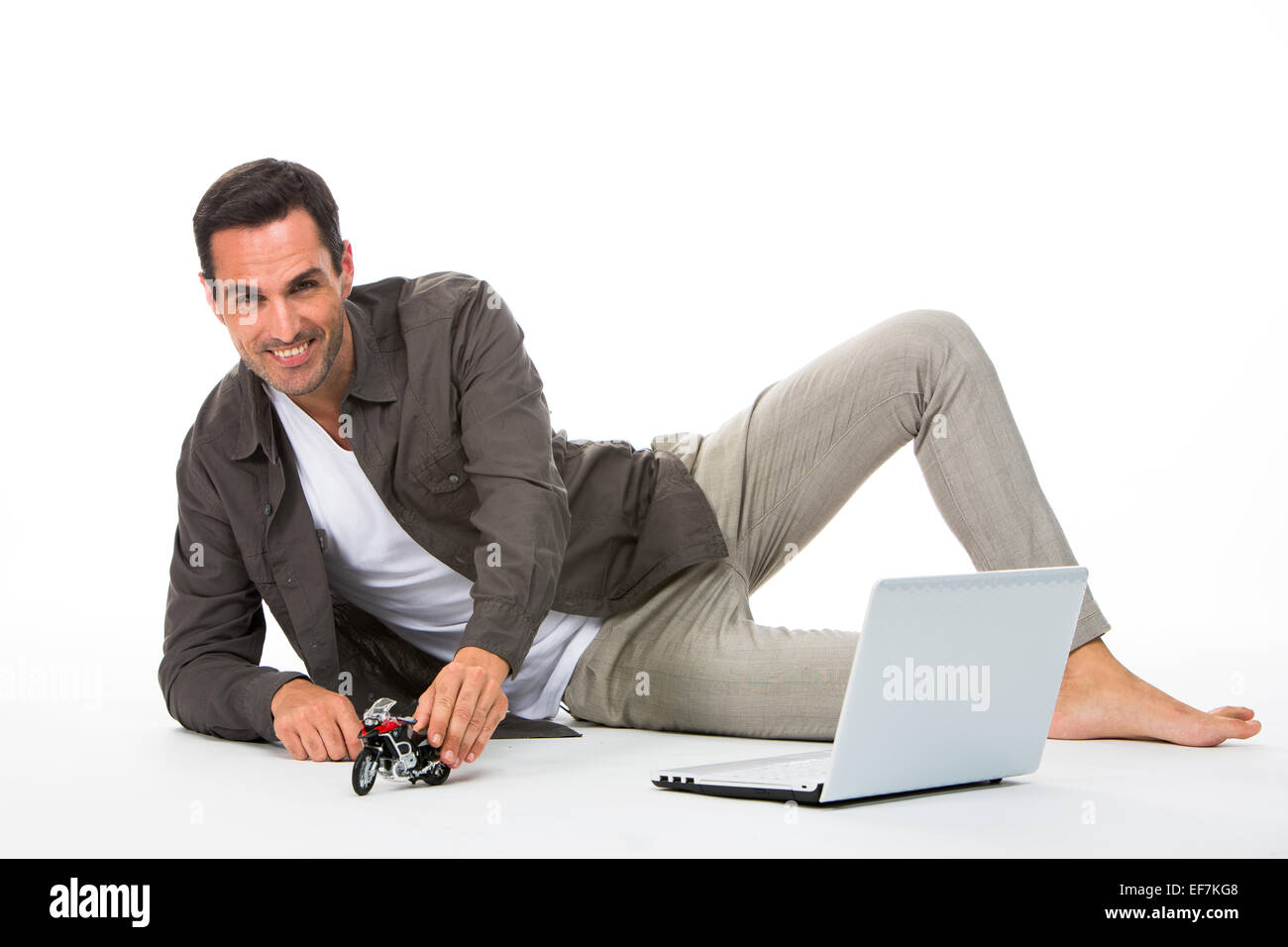 Mann auf dem Boden, lächelnd in die Kamera, die mit einem Motorrad Modell und einem Laptop neben ihm spielen Stockfoto