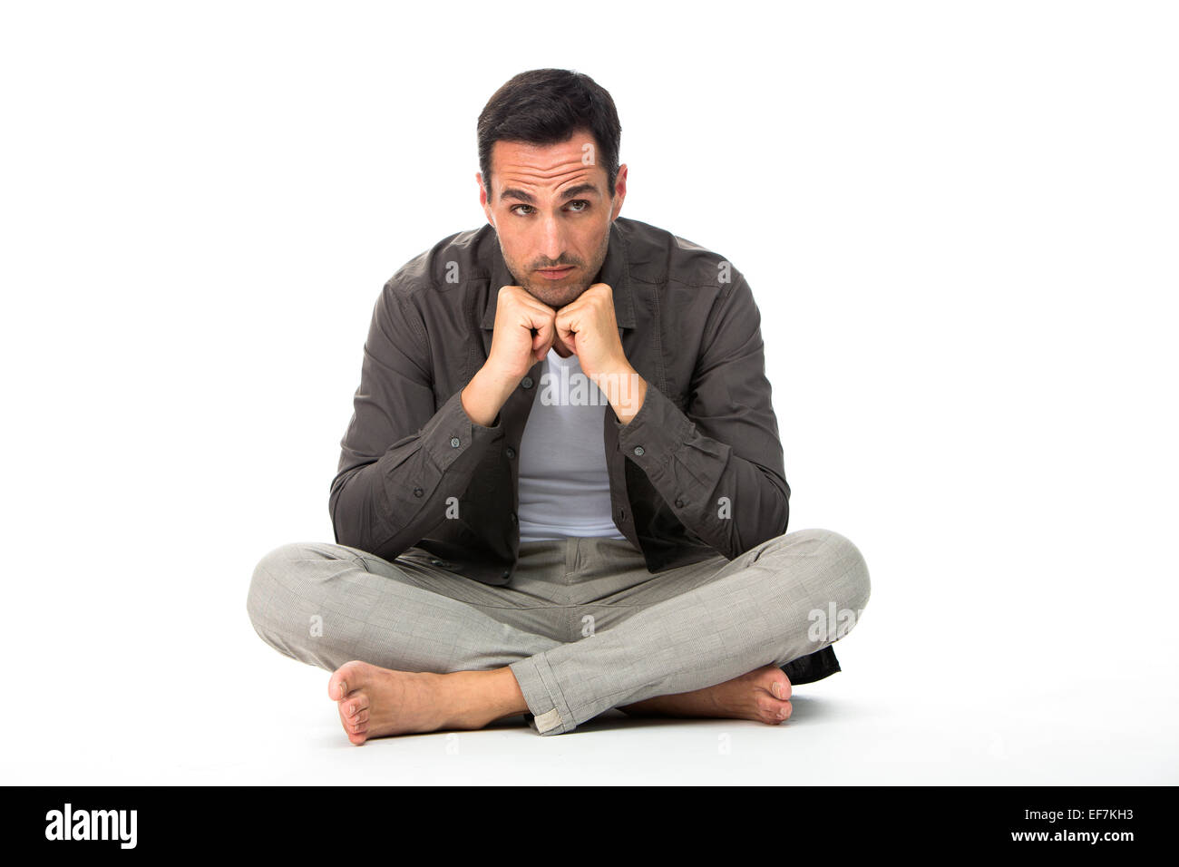 Nachdenklicher Mann sitzen auf dem Boden mit den Händen unter dem Kinn Stockfoto