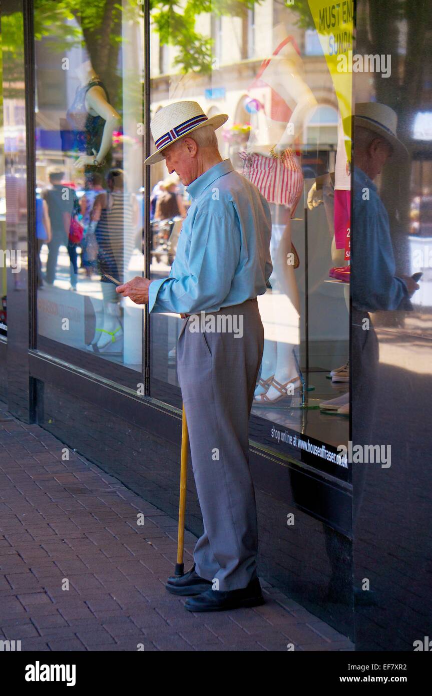 Elegant gekleidete Greis mit einem Gehstock mit einem Smartphone. Stockfoto