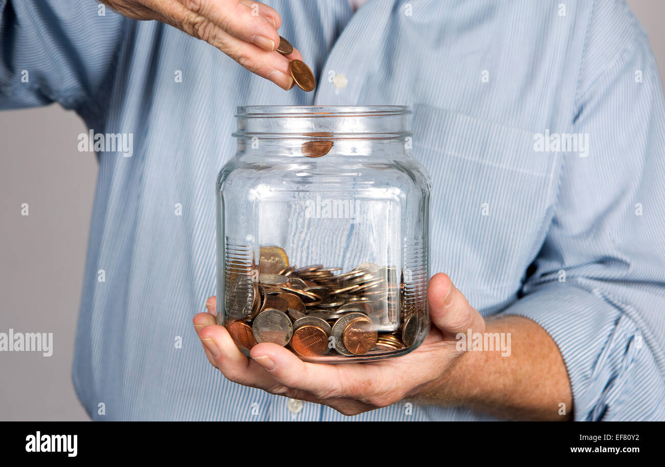 Mann wirft Geld in ein Glas für ein Sparkonto. Stockfoto