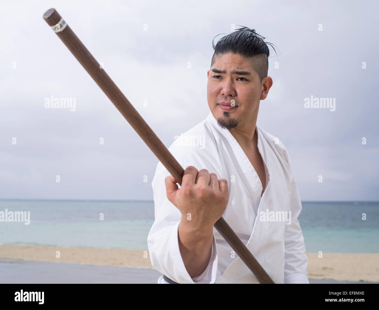 Fumiya Matayoshi mit Bo Personalschulung in Kobudo / Karate am Strand in Okinawa Japan. Stockfoto