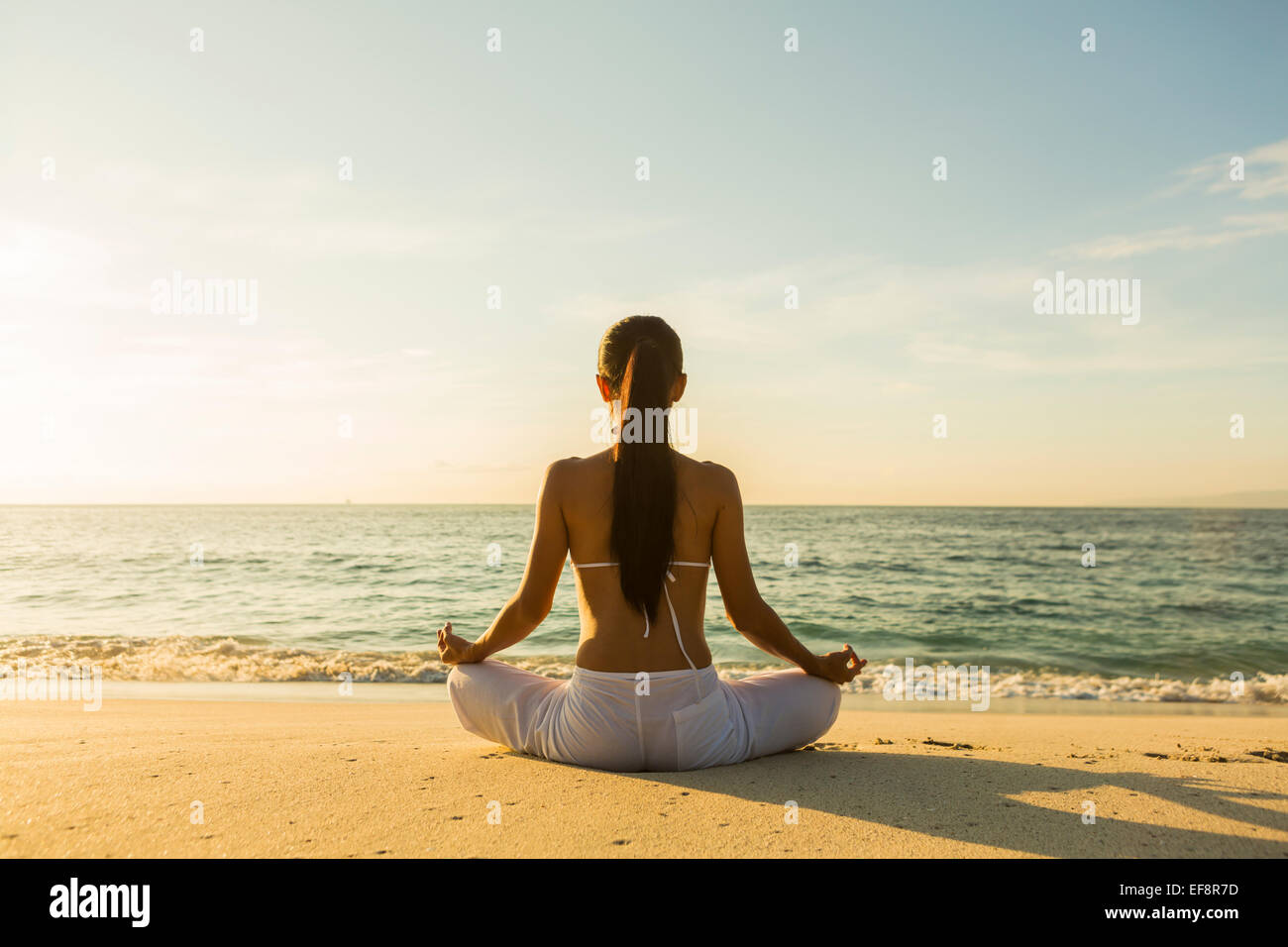 Rückansicht einer Frau, die am Strand am Rande des Wassers sitzt und meditiert, Singapur Stockfoto